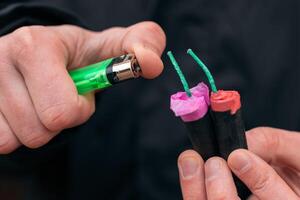 Setting Fire to the several Firecrackers. Man in Black Clothes Lighting Up Two Petards at the Same Time. Firing Up the Pyrotechnic with Green Gas Lighter Outdoors photo