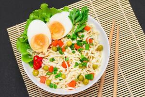 Beautiful Noodle Dish with Green Pea, Carrot, Eggs, Red Hot Pepper and Greens on Sushi Mat. Instant Noodles with Vegetables photo