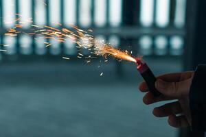 Burning Firecracker with Sparks. Guy Holding a Petard in a Hand. Loud and Dangerous New Year's Entertainment. Hooliganism with Pyrotechnics. Noise of Firecrackers in Public Places photo