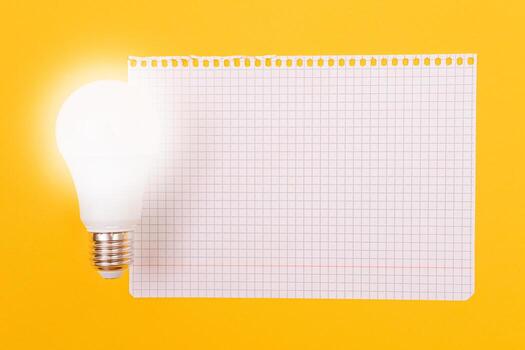 A Power Saving Lamp with Notepad Lying on Yellow Table, Blank Template with Copy Space - Top View, Flat Lay photo