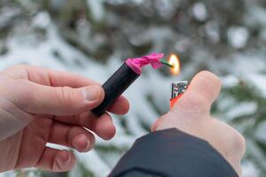 Guy Sets Fire to the Flash Noise Firecracker Outdoors in Winter at Daytime. Loud and Dangerous New Year's Entertainment. Hooliganism with Pyrotechnics. Noise of Petards in Public Places photo