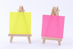 Two Wooden Easels Miniature with Blank Colored Square Canvas or Memo Paper - Mockup. Mini Wooden Stand with Clean Artboard on White Background, Copy Space photo