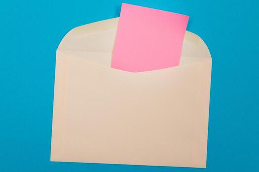 Beige Envelope with Blank Pink Sheet of Paper Inside, Lying on Blue Background - Mock Up with Copy Space. Receiving Mail or Notice, Sending Postcard - Top View, Flat Lay photo