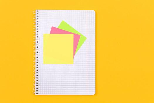 A Notepad with Sticky Notes Lying on Yellow Table - Blank Template. Top View, Flat Lay photo