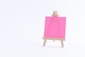 Wooden Easel Miniature with Blank Colored Square Canvas or Memo Paper - Mockup. Mini Wooden Stand with Clean Artboard on White Background, Copy Space photo