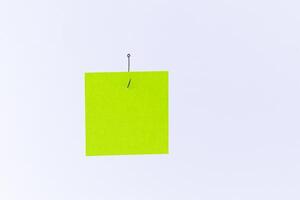 Mockup of a Blank Green Memo Paper with Copy Space Hanging on a Fishing Hook Against the White Background. Reminder or To Do List. Sticky Note Template photo