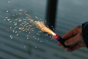 Burning Firecracker with Sparks. Guy Holding a Petard in a Hand. Loud and Dangerous New Year's Entertainment. Hooliganism with Pyrotechnics. Noise of Firecrackers in Public Places photo