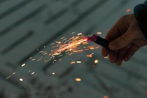 Burning Firecracker with Sparks. Guy Holding a Petard in a Hand. Loud and Dangerous New Year's Entertainment. Hooliganism with Pyrotechnics. Noise of Firecrackers in Public Places photo