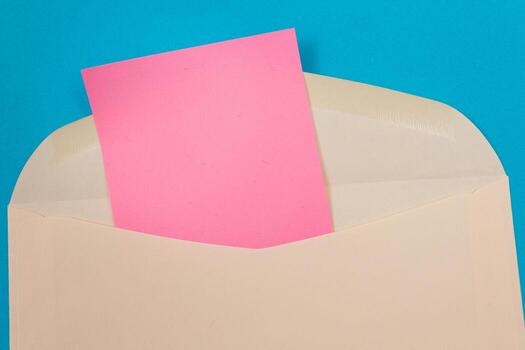 Beige Envelope with Blank Pink Sheet of Paper Inside, Lying on Blue Background - Mock Up with Copy Space. Receiving Mail or Notice, Sending Postcard - Top View, Flat Lay photo