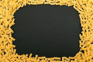 A Frame Made from Uncooked Fusilli Pasta Scattered on Black Table - Mock Up. Raw and Dry Macaroni. Unhealthy and Fat Food. Italian Culture photo