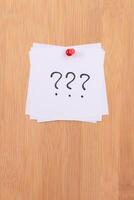 White Sticky Notes with Three Question Marks Pinned to the Wooden Message Board. To Do List Reminder in the Office. Memo Note at Work photo