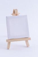 Wooden Easel Miniature with Blank White Square Canvas for Artists and Painters - Mockup. Mini Wooden Stand with Clean Artboard on White Background, Copy Space photo