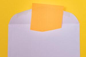 Violet Envelope with Blank Orange Sheet of Paper Inside, Lying on Yellow Background - Mock Up with Copy Space. Receiving Mail or Notice, Sending Postcard - Top View, Flat Lay photo