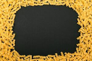 A Frame Made from Uncooked Fusilli Pasta Scattered on Black Table - Mock Up. Raw and Dry Macaroni. Unhealthy and Fat Food. Italian Culture photo