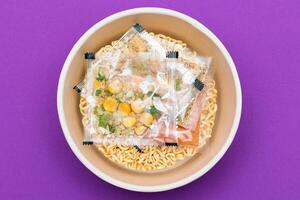 Opened Package with Uncooked Instant Noodles on Violet Background. Raw Pasta. Dry Asian Fast Food. Quick Lunch photo