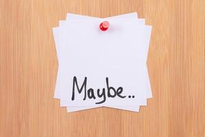 MAYBE.. - White Sticky Notes with Written Word MAYBE, Pinned to the Wooden Message Board. To Do List Reminder in the Office. Memo Note at Work photo