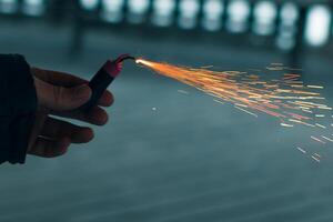 Burning Firecracker with Sparks. Guy Holding a Petard in a Hand. Loud and Dangerous New Year's Entertainment. Hooliganism with Pyrotechnics. Noise of Firecrackers in Public Places photo