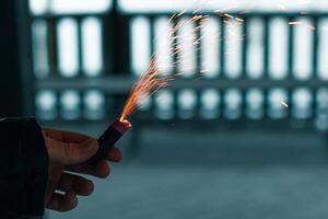 Burning Firecracker with Sparks. Guy Holding a Petard in a Hand. Loud and Dangerous New Year's Entertainment. Hooliganism with Pyrotechnics. Noise of Firecrackers in Public Places photo