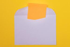 Violet Envelope with Blank Orange Sheet of Paper Inside, Lying on Yellow Background - Mock Up with Copy Space. Receiving Mail or Notice, Sending Postcard - Top View, Flat Lay photo