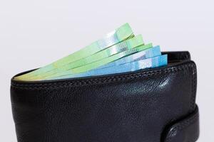 Black Leather Men Wallet with Euro Banknotes Inside on White Background. A Purse Full of Money Symbolizing Wealth, Success and Social Status photo
