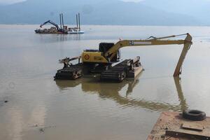 Semarang, 7 September 2022 - Excavator dredging mud in a Rawa Pening lake with mountains in the background. photo