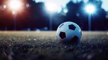 close up view of soccer ball resting on grassy field, illuminated by bright stadium lights in background, creating exciting atmosphere for game photo