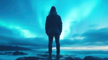 person stands on rocky shore, gazing at mesmerizing northern lights illuminating night sky with vibrant colors. serene atmosphere evokes sense of wonder and tranquility photo