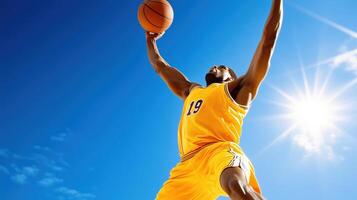 basketball player in yellow jersey performs slam dunk against bright blue sky, showcasing athleticism and energy. sun shines brightly, enhancing dynamic scene photo