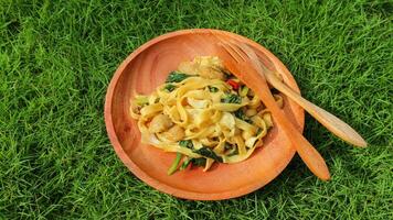 Kwetiaw or Kwetiau is Chinese food which is popular in Indonesia, cooked by frying added with chicken, seafood and complementary vegetables. Served in wooden plate on green grass background. photo