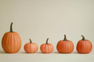 Five Orange Pumpkins of Varying Sizes on a Light Beige Background photo