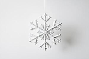A Glittery White Snowflake Ornament Hanging Against a White Background photo