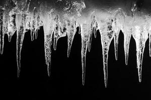 Icicles hanging from a roof, against a dark background. photo