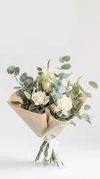 Elegant bouquet of white roses and eucalyptus beautifully wrapped in paper. Professional florist photo