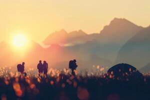 Sunset camping trip with silhouettes of hikers and tent in a meadow. Blurred mountains on a background. photo