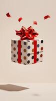 Gift box with polka dot wrapping paper and red ribbon floating on beige background photo