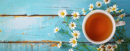 Cup of chamomile tea with fresh flowers on rustic blue wooden background, relaxing and wellness vibe photo