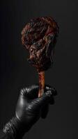 Chef's hand in a black glove holding a grilled tomahawk steak on a dark background for meat lovers photo