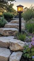 LED outdoor light post illuminating a garden path with flowering plants and decorative stones photo