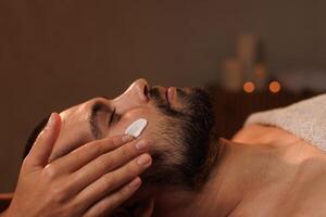 Cosmetician applying cosmetic cream of man in spa photo