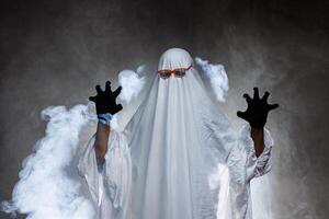 man in scary ghost costume in smoke on grey mysterious background in studio. Minimal halloween ghost concept. photo