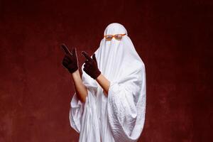 Man in ghost costume pointing at something on gray background in smoke with space for text. Halloween celebration photo