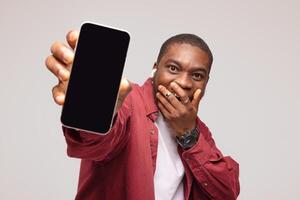 Surprised african young man showing smartphone screen and rejoicing at success, on white background, photo