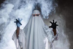 man in scary ghost costume in smoke on grey mysterious background in studio. Minimal halloween ghost concept. photo