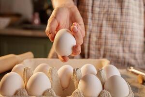 Heart shaped egg on frying pan, kitchen table and egg carton in background, top view photo