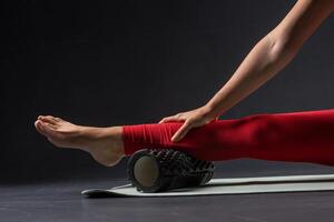 physiotherapy massage, woman with yoga roller on floor for leg tension on dark background photo