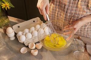 Close-up of female hands beating eggs with a hand whisk in a transparent bowl against photo