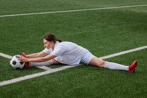 A young female soccer player stretches on a soccer field and reaches for a soccer ball photo