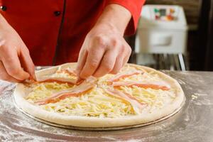 Chef adding bacon to cheese pizza photo
