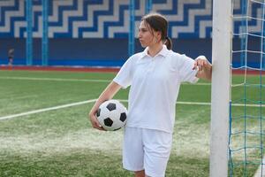 A female soccer player holds a soccer ball and leans against a goal post on a soccer field. photo