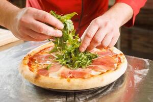 Chef adding fresh arugula to prosciutto pizza photo